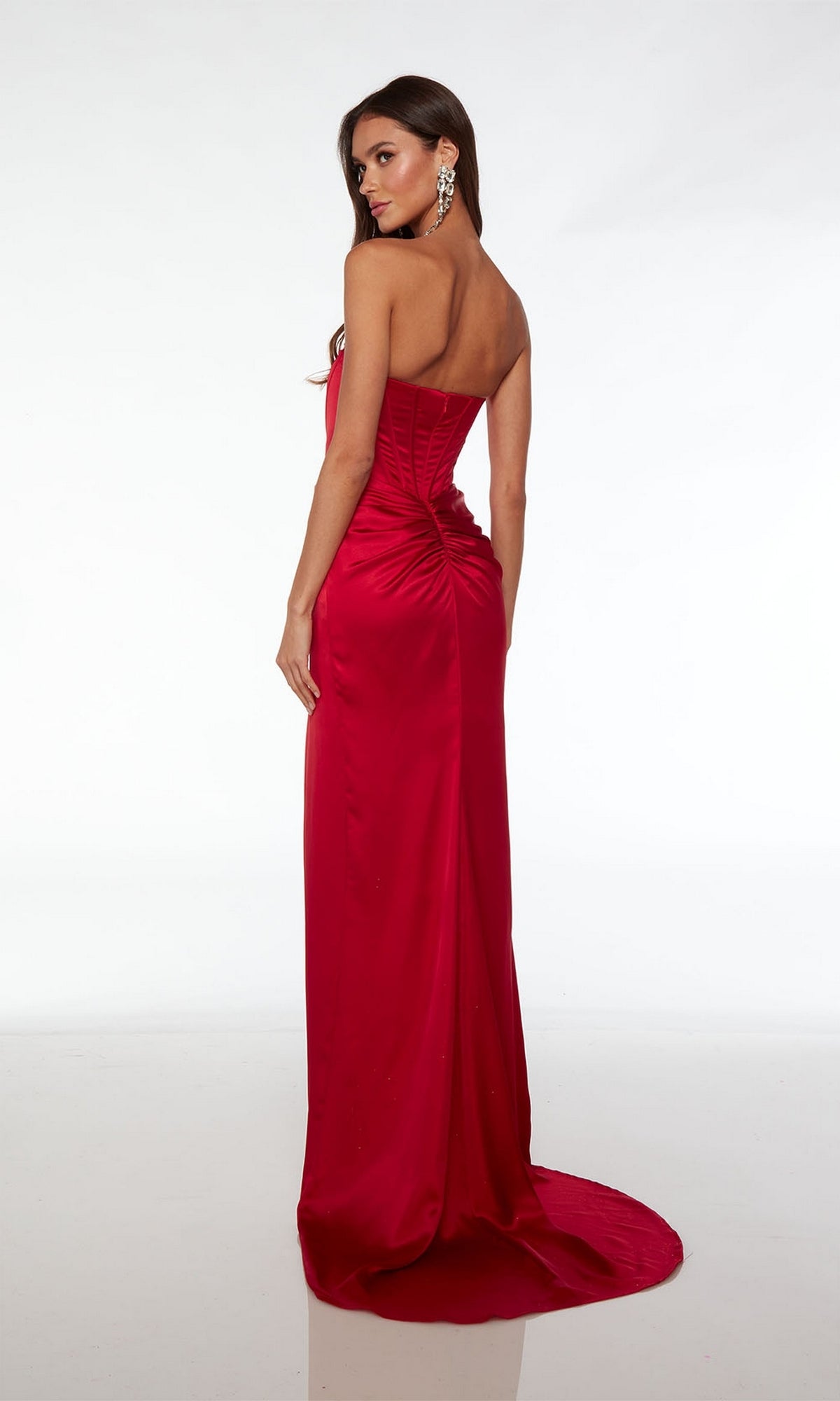 A woman wears the Alyce Strapless Long Corset Prom Dress 61489, featuring a satin finish, corset-style bodice, and ruched back detail, as she stands facing away and looks over her shoulder.